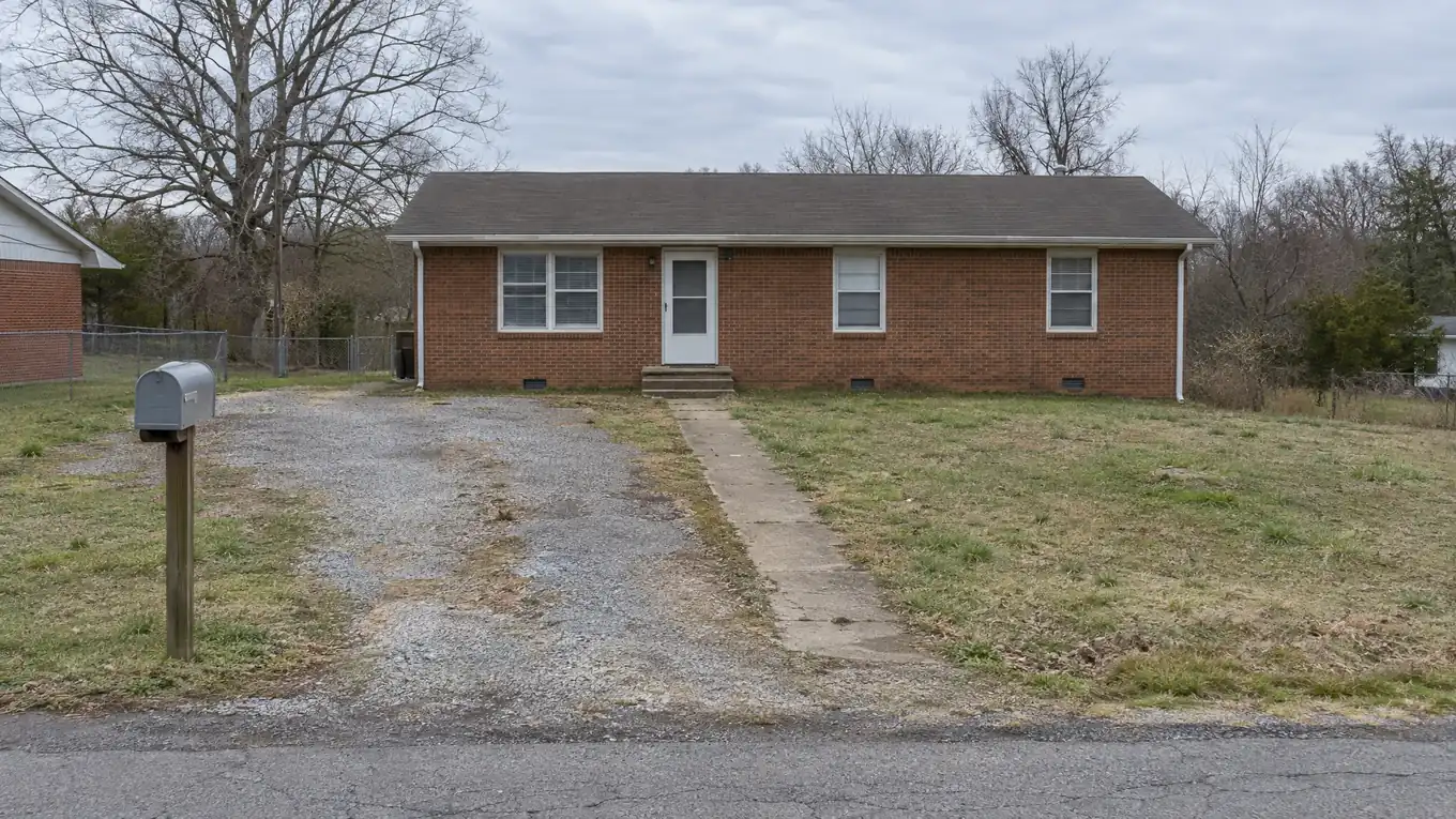 Plain gravel and cracked asphalt driveway with a basic metal mailbox before the makeover